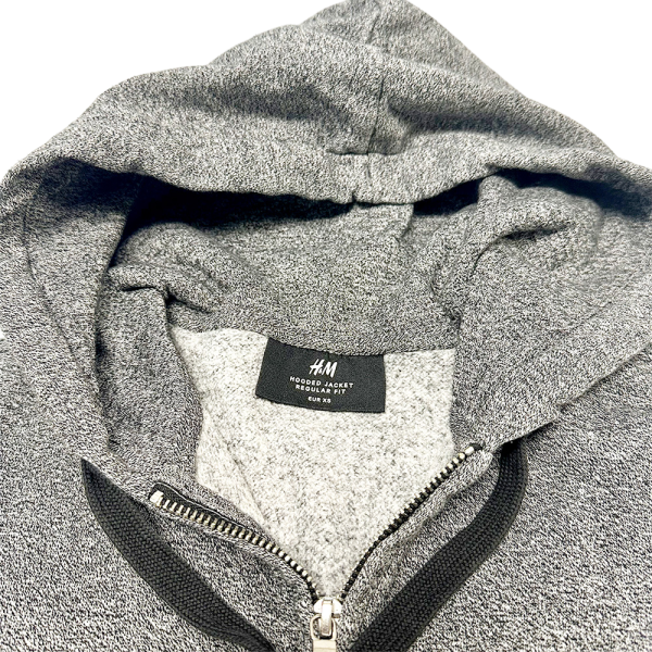 Sudadera con cremallera gris de H&M, detalle de la capucha y etiqueta de talla, vista desde arriba.