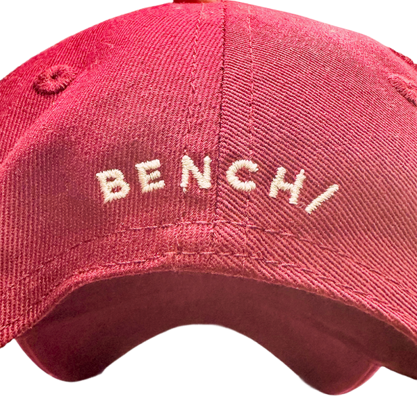 Close-up of a red Bench baseball cap with white embroidered logo, stylish and casual headwear option.