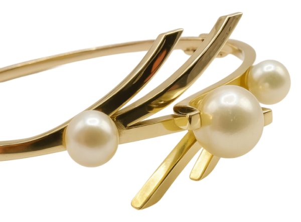 Gold bracelet featuring a modern bangle design with three elegant pearls on a polished gold band.